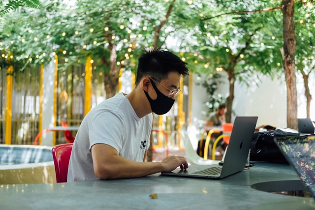 a man wearing a black mask working with a laptop